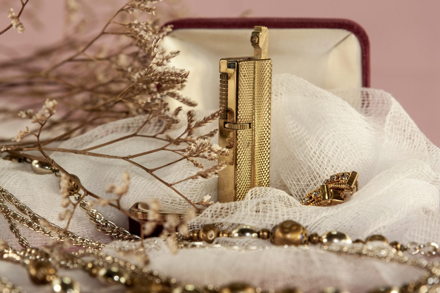 Close-up of luxurious gold jewelry and dry flowers with a soft, artistic ambiance.